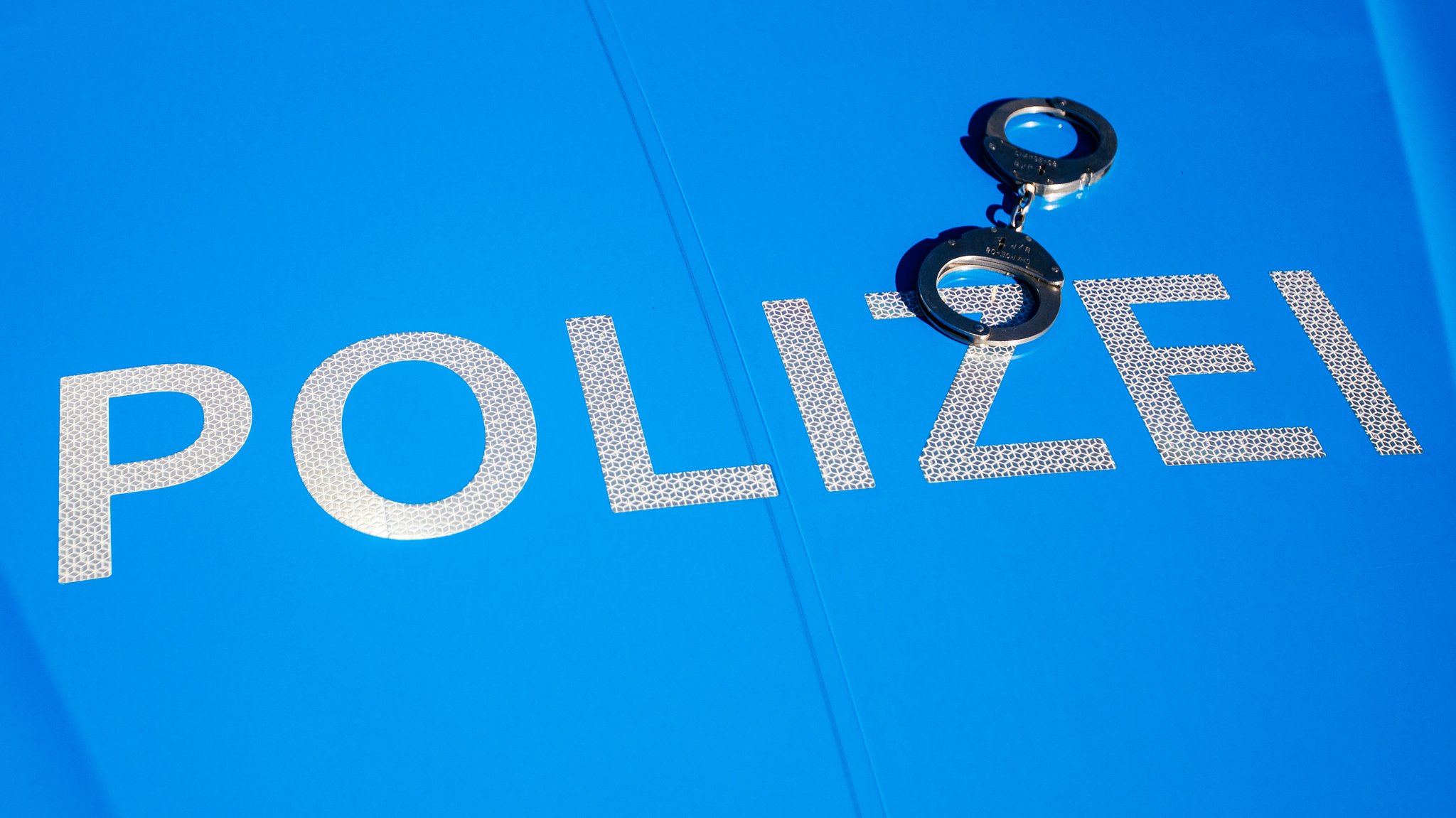 Handschellen liegen auf der Motorhaube eines blauen Polizeiautos 