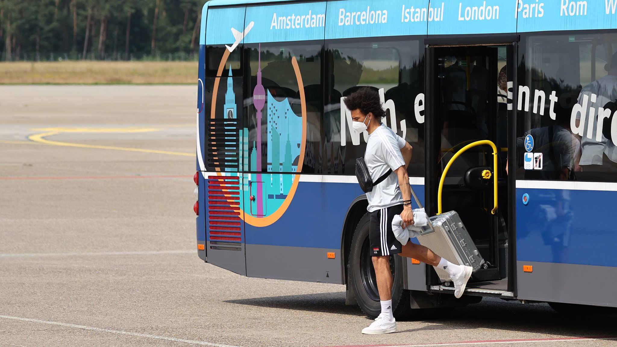 Leroy Sane steigt aus einem Bus, in der Hand einen silbernen Rollkoffer.