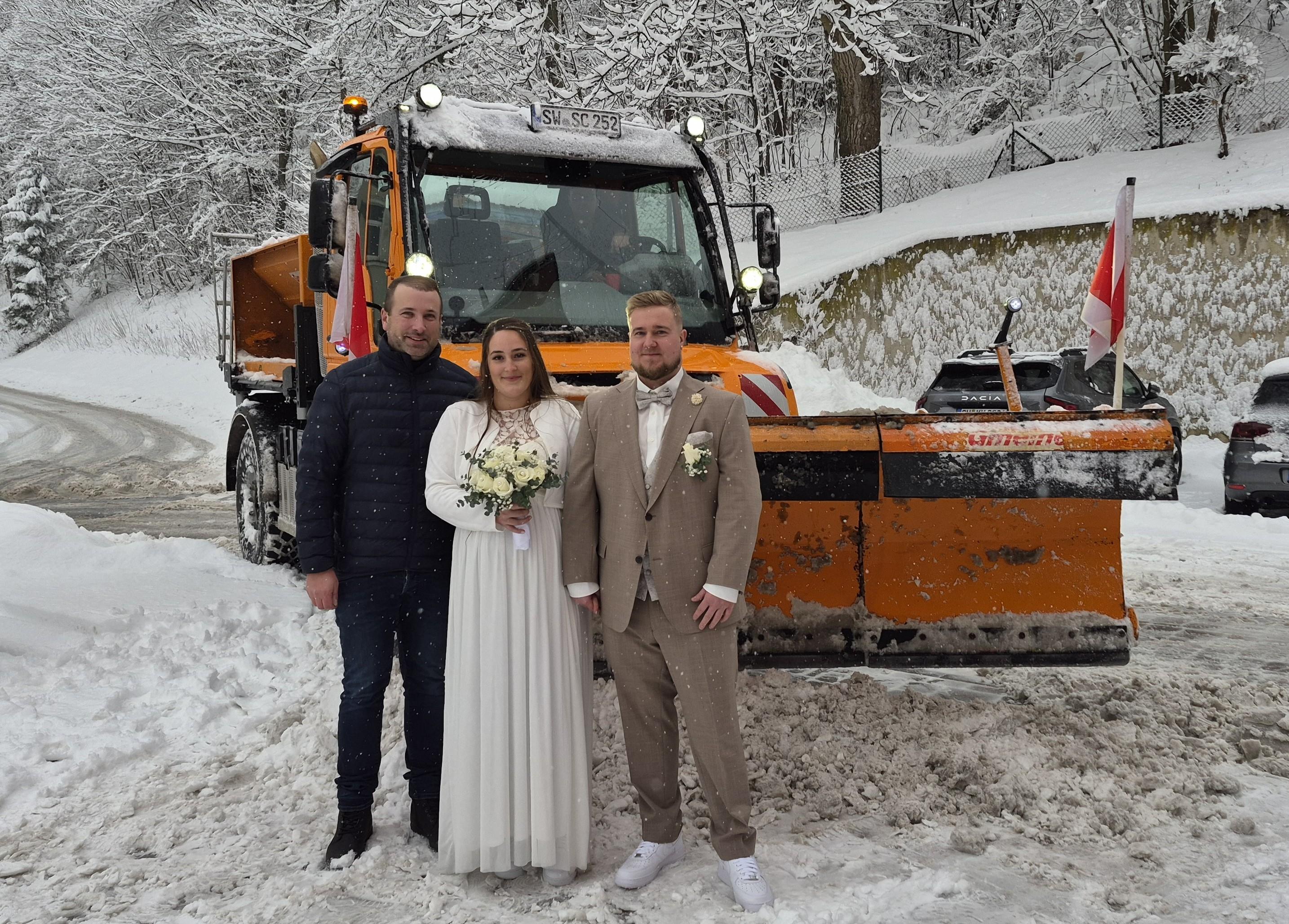 Drei Menschen stehen vor einem Schneepflug 