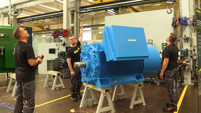 Drei Mitarbeiter von Siemens stehen um einen großen Motor