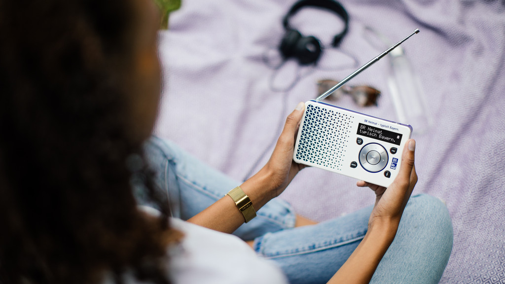 Eine Frau sitzt mit einem DAB+ - Radio auf einer Picknickdecke