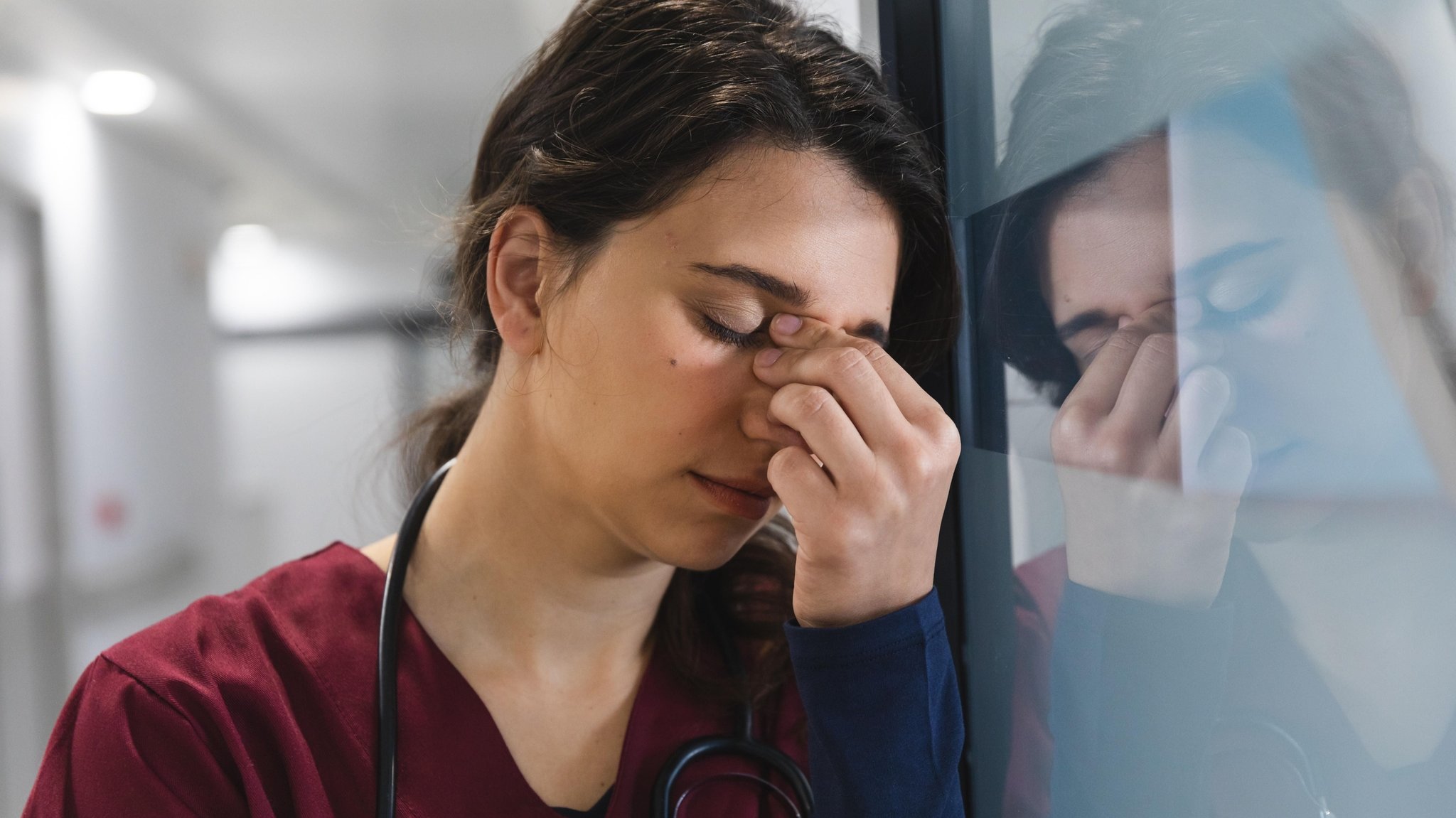 Eine junge Ärztin in einem Krankenhaus lehnt sich erschöpft an eine Wand (Symbolbild)