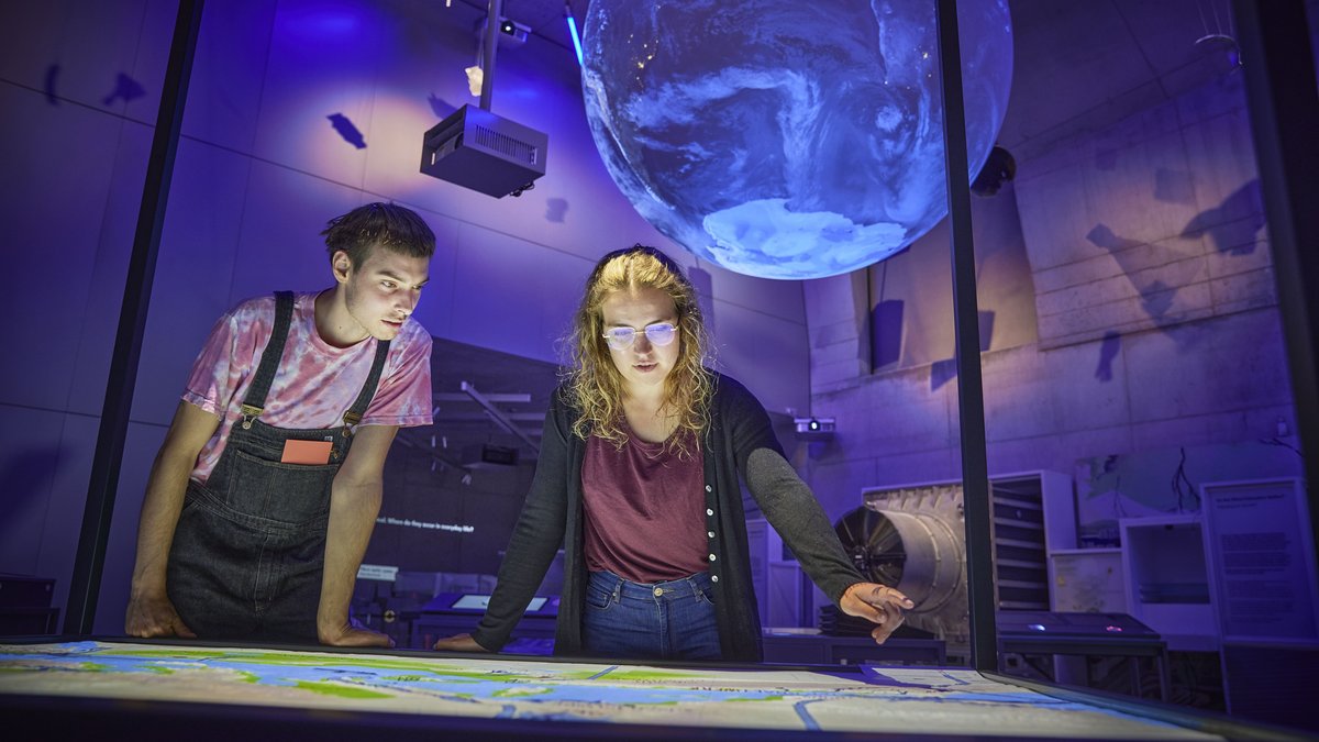 Ein Mann und eine Frau besichtigen eine Karte, darüber schwebt ein blau leuchtendes Modell der Erde.
