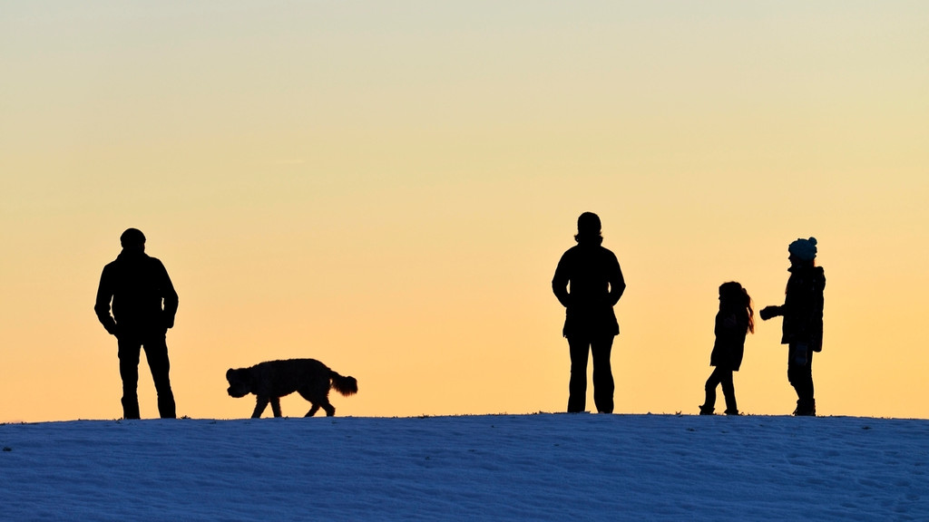 Silhouetten von Vater, Mutter, Kind und einem Mann mit Hund vor Sonnenuntergang