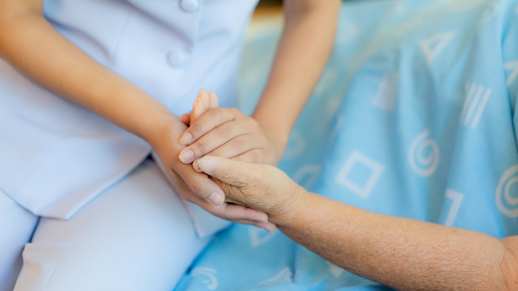 Nahaufnahme der Hände einer Pflegekraft, die die Hand einer älteren Person hält.