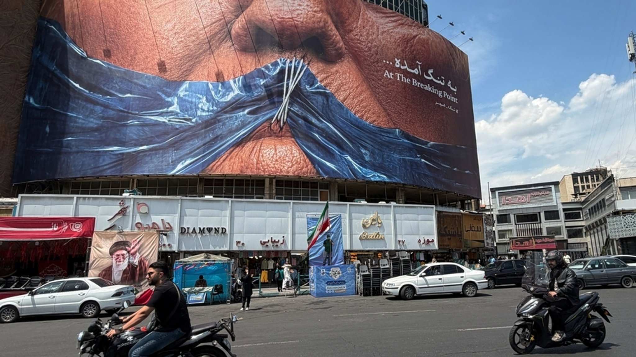 02.05.2026, Iran, Teheran: Fahrzeuge fahren an einem Plakat mit einer Grafik vorbei, die die Umrisse der Straße von Hormus und US-Präsident Donald Trump mit zugenähten Lippen auf einem Platz in der Innenstadt von Teheran zeigt.