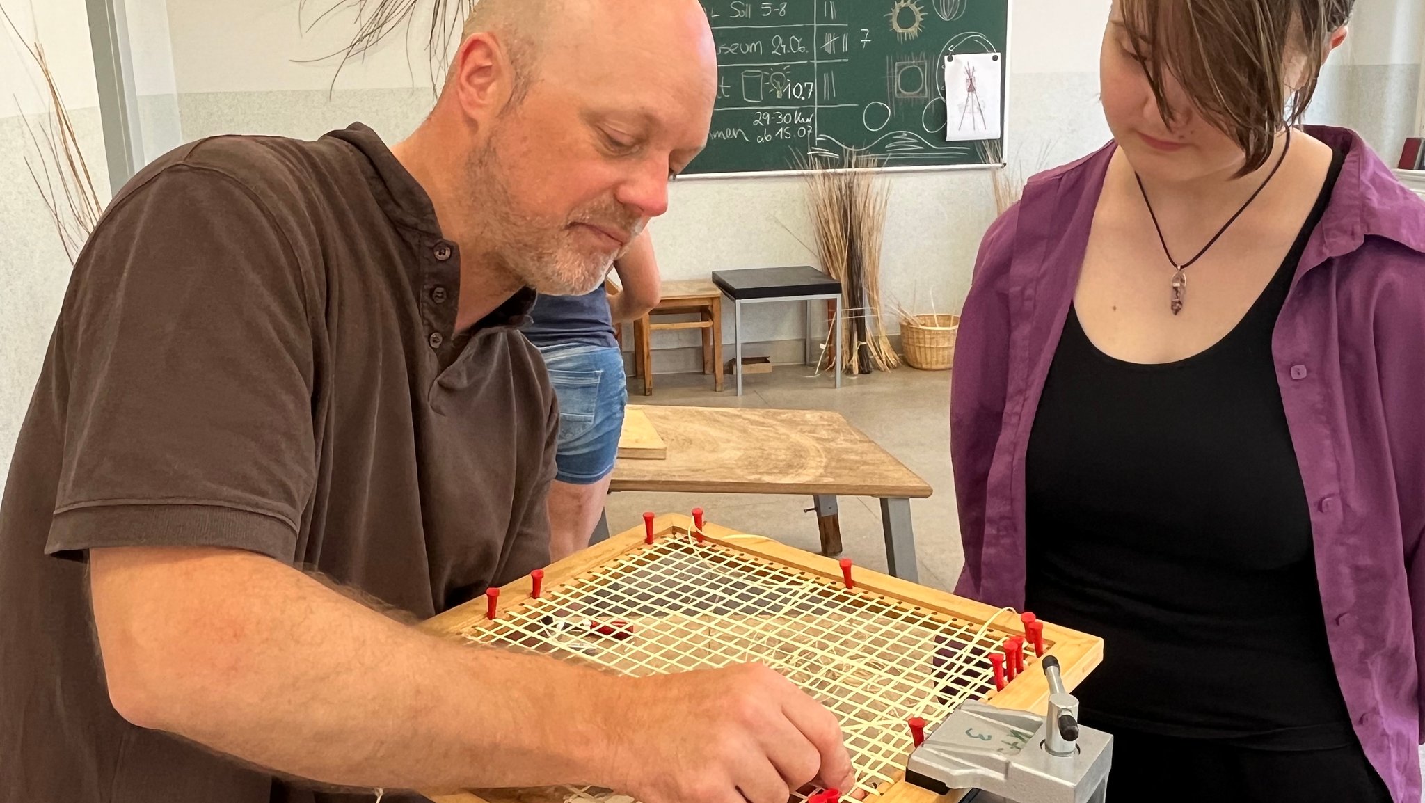 Ein Mann zeigt einer jungen Frau Handgriffe beim Flechten