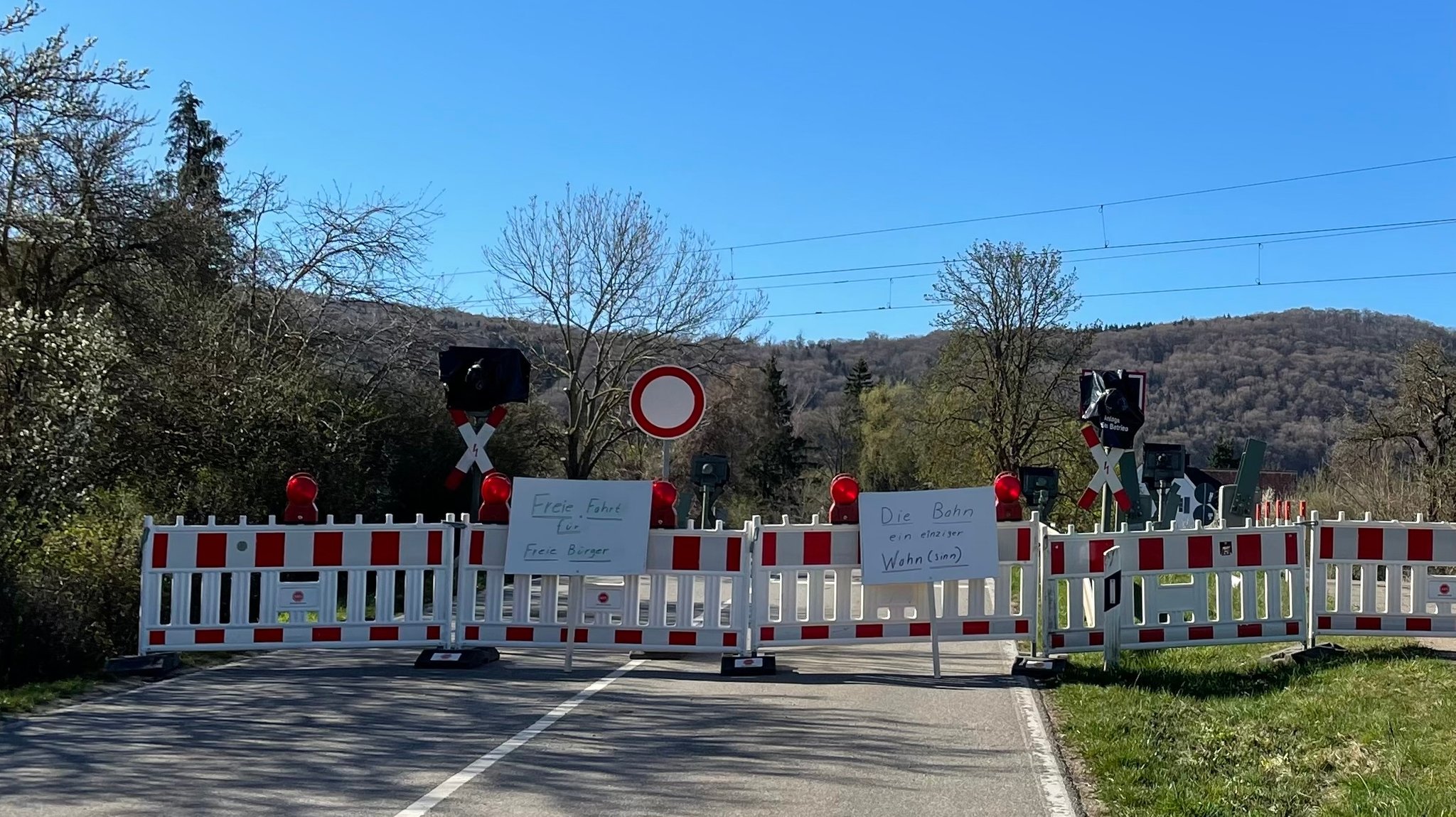 Warnbaken und Protestschilder vor einem Bahnübergang.