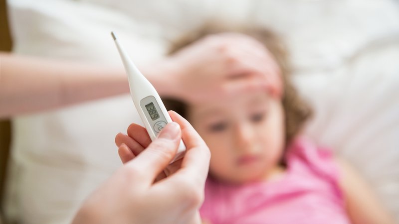 Ein Fieberthermometer mit einem Kind im Hintergrund.