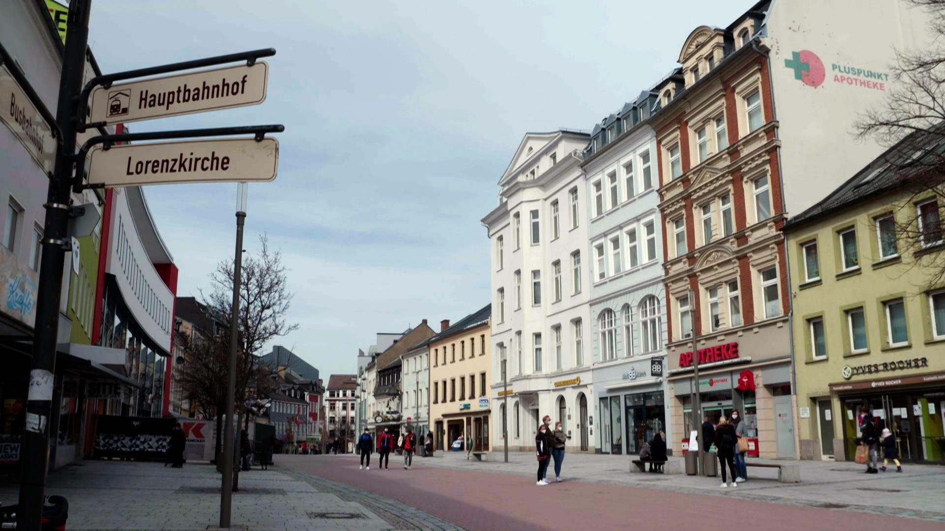 Durch eine Fußgängerzone gehen Menschen an Geschäften vorbei. 