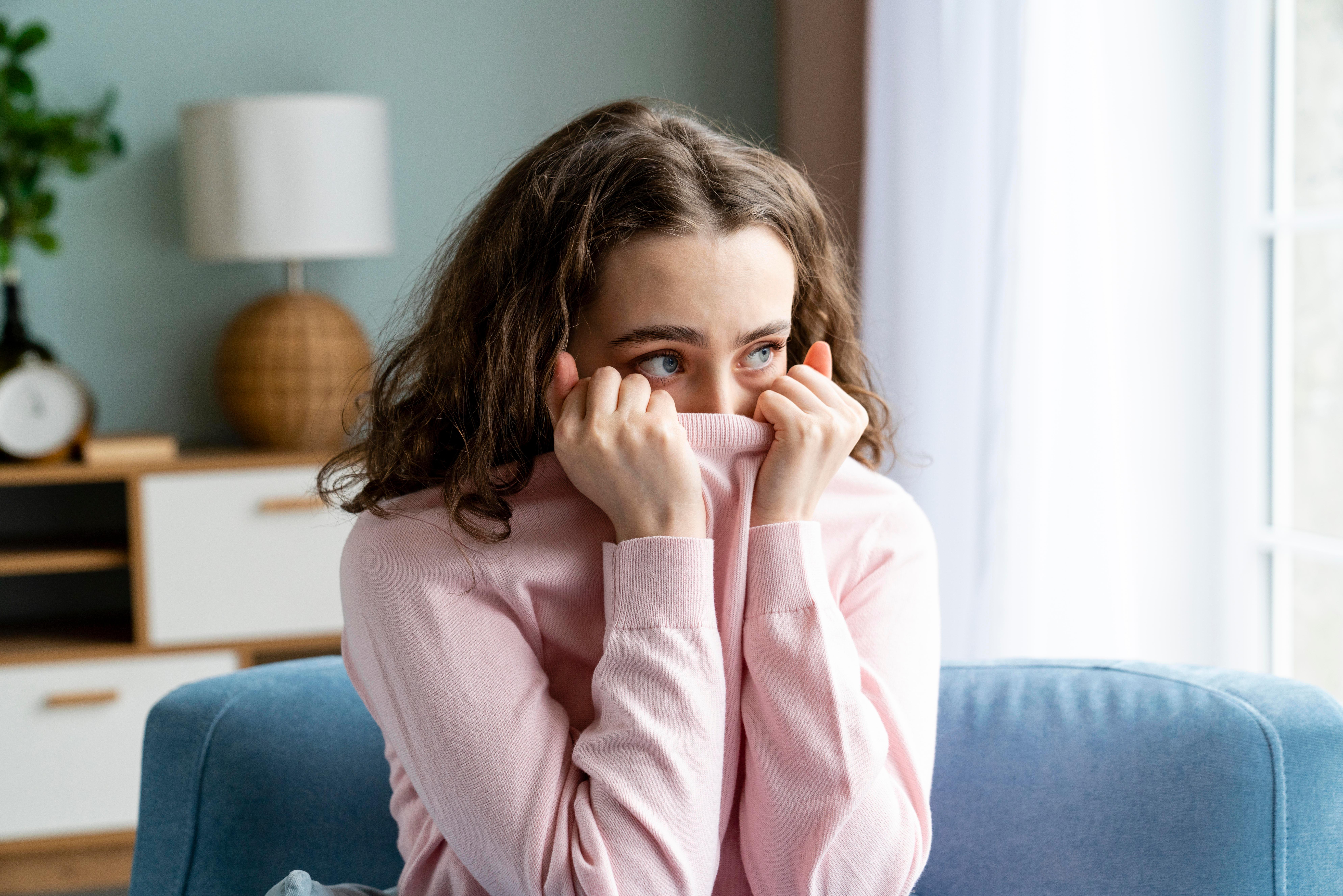 Ängstliche Frau zieht ihren Pulli über Mund und Nase