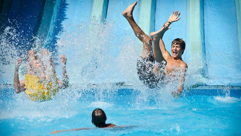 Drei Kinder haben in einem Freibad Spaß auf der Wasserrutsche. | Bild: stock.adobe.com/starsstudio Drei Kinder haben in einem Freibad Spaß auf der Wasserrutsche.