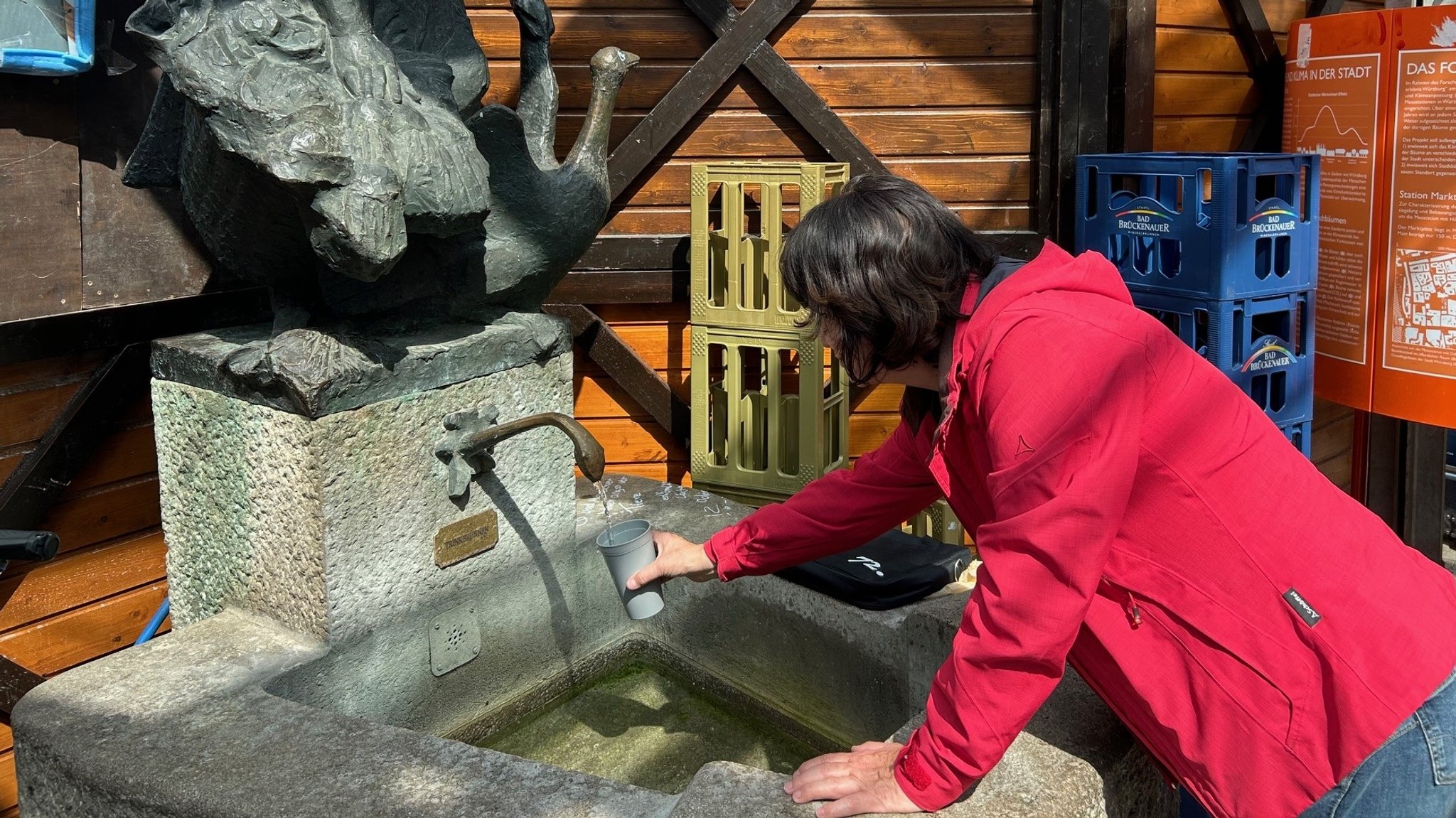 Eine Würzburgerin füllt am Rande des Würzburger Weindorfs am Unteren Markt ihren Becher an einem Trinkwasserbrunnen