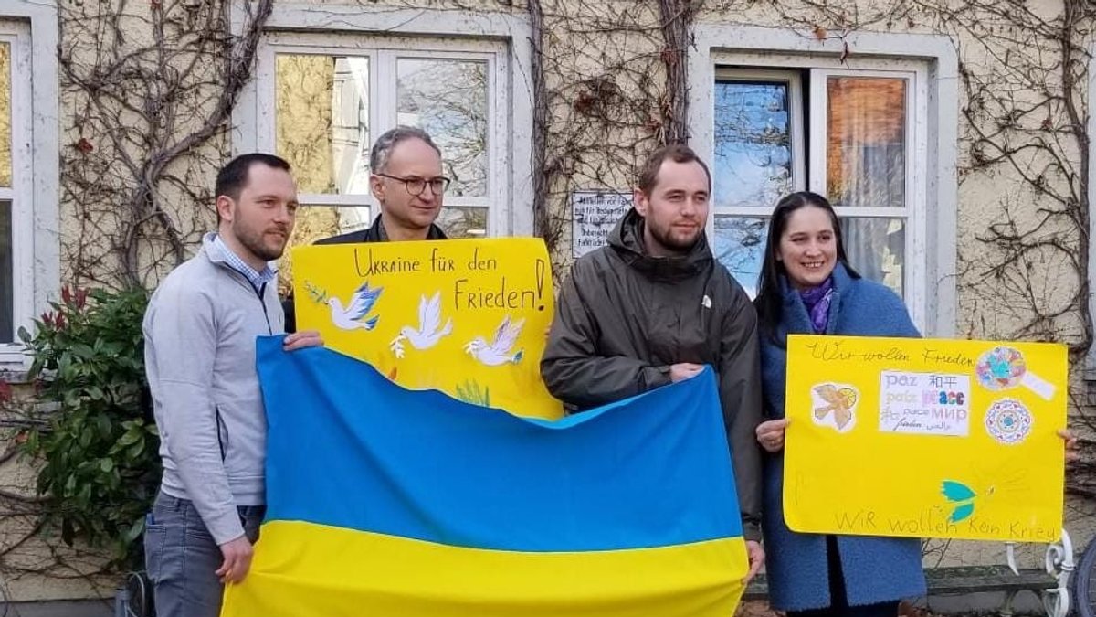 Drei Männer und eine Frau halten die ukrainische Fahne und Transparente in der Hand