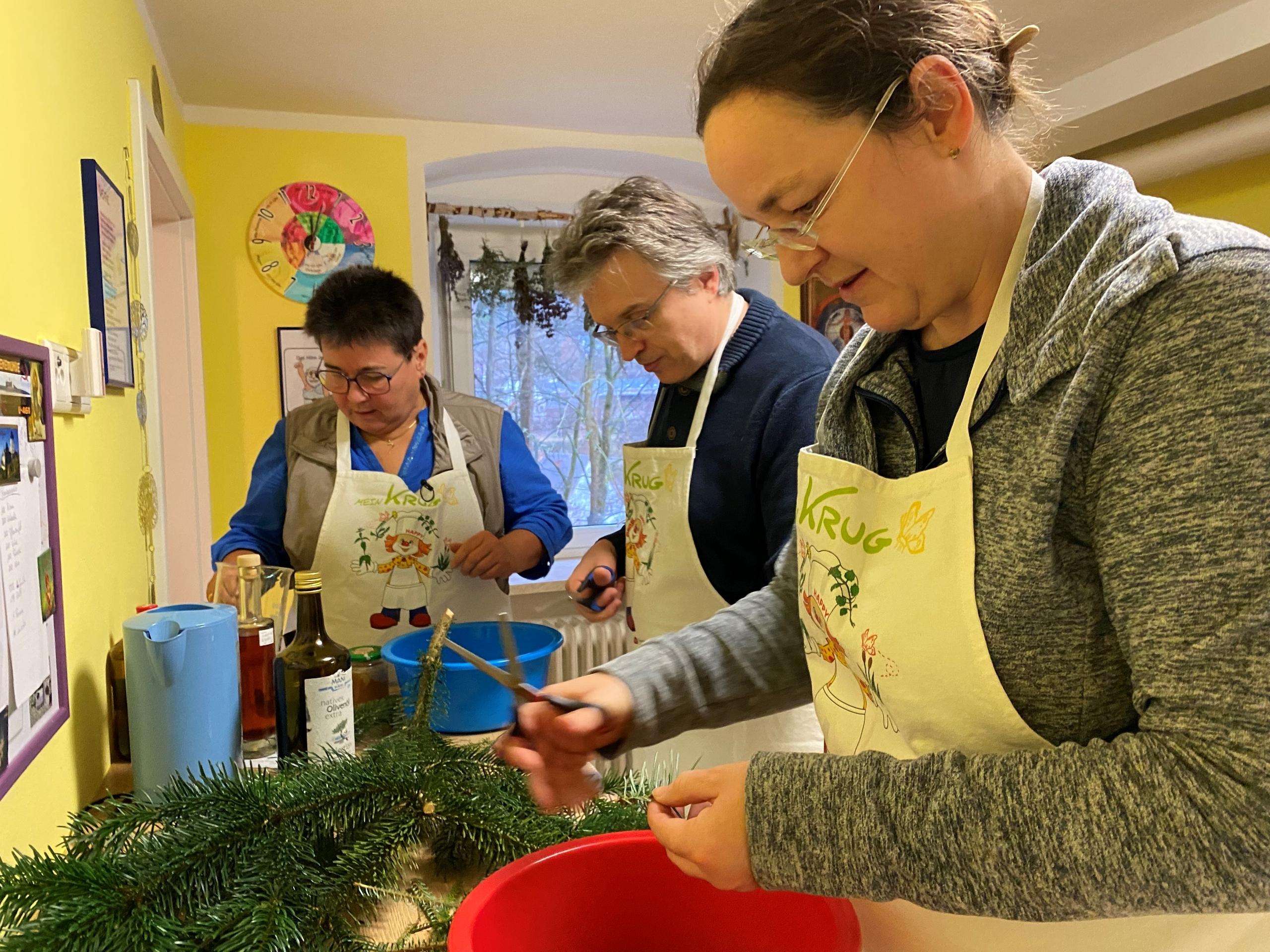Drei Menschen schneiden Nadeln von Tannenzweigen. 