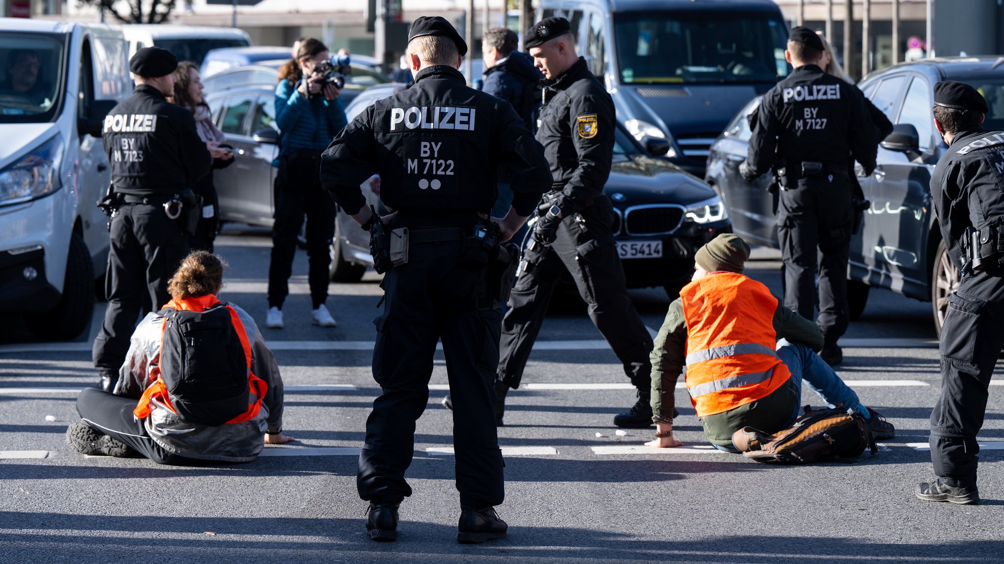 München, 07.11.22: Polizeibeamte stehen neben Klimaaktivisten, die sich am Stachus auf die Fahrbahn geklebt und somit die Straße blockiert haben.