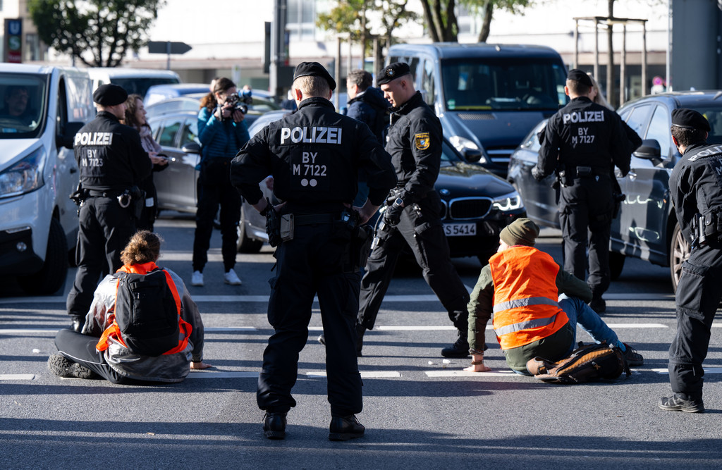 München, 07.11.22: Polizeibeamte stehen neben Klimaaktivisten, die sich am Stachus auf die Fahrbahn geklebt und somit die Straße blockiert haben.