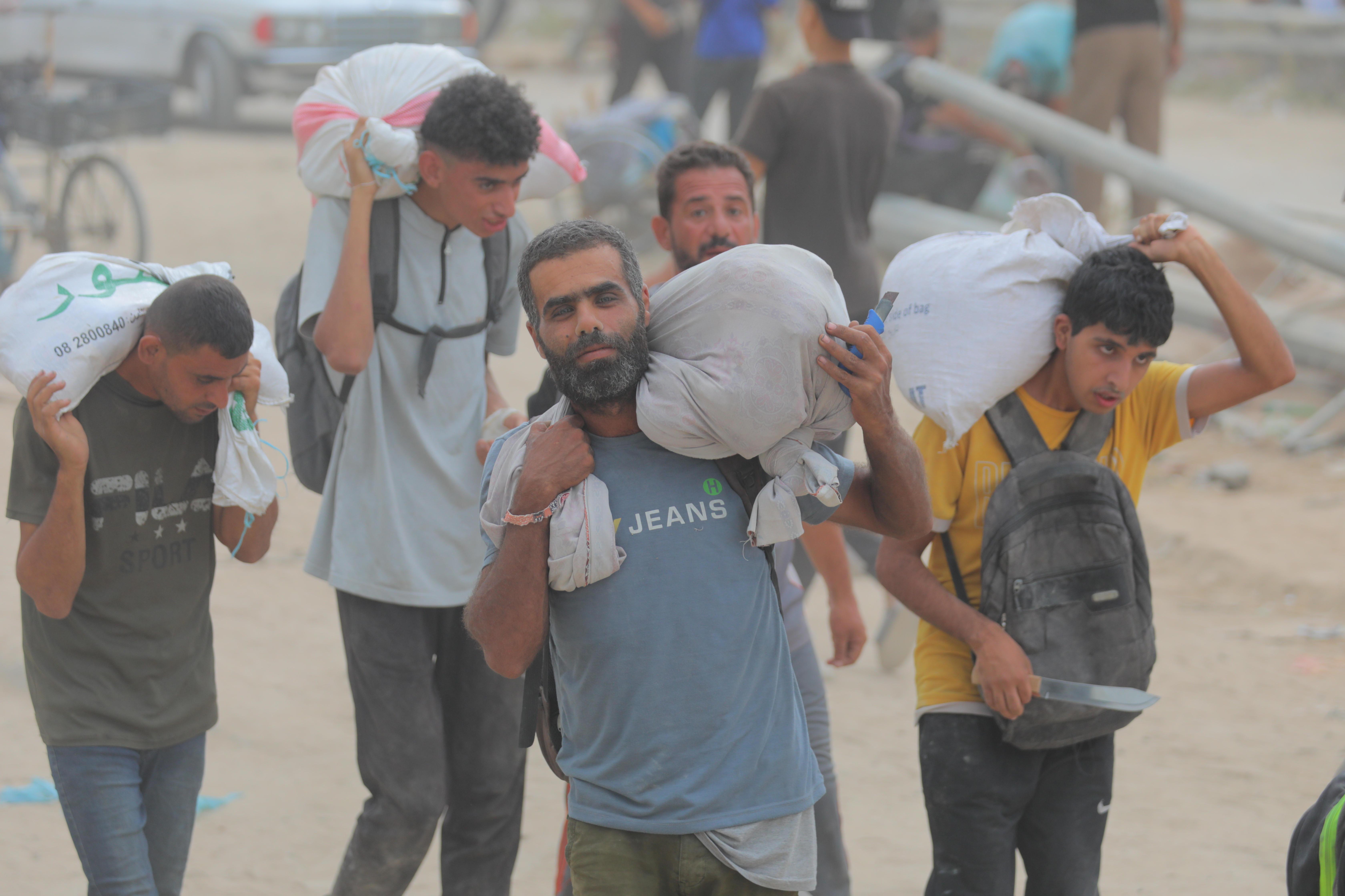 Mehren Männer tragen weiße Säcke mit Hilfsgütern auf ihren Schultern. 