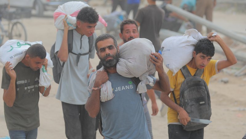 Mehren Männer tragen weiße Säcke mit Hilfsgütern auf ihren Schultern. | Bild: picture alliance / Anadolu | Hassan Jedi Mehren Männer tragen weiße Säcke mit Hilfsgütern auf ihren Schultern.