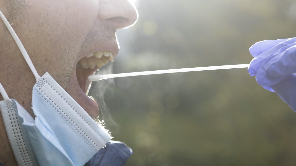 Corona-Teststäbchen wird in den Mund eines Mannes eingeführt.