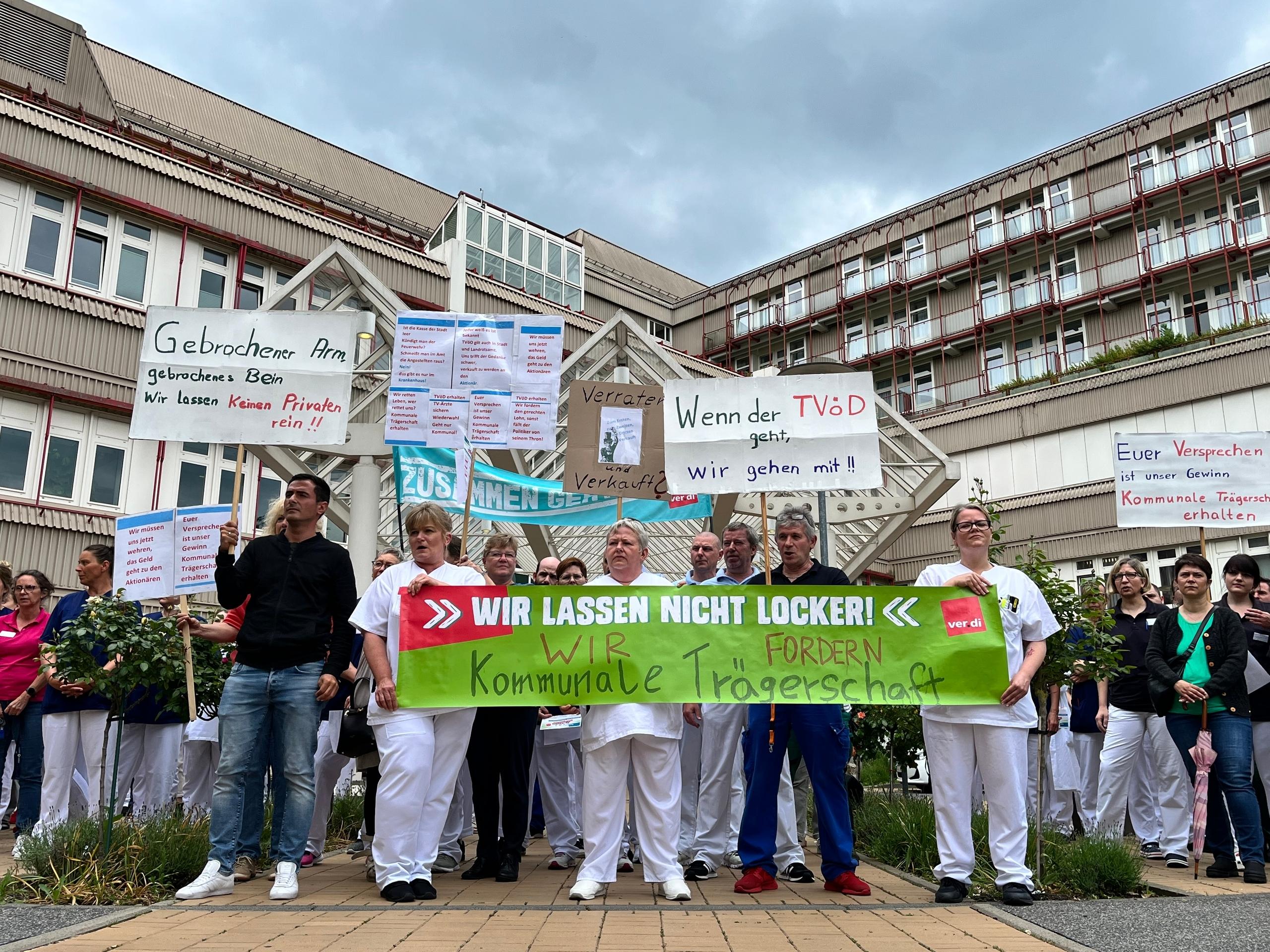 Krankenhaus-Mitarbeiter halten Transparente in die Höhe, auf denen steht unter anderem: "Wir lassen nicht locker, wir fordern kommunale Trägerschaft". 