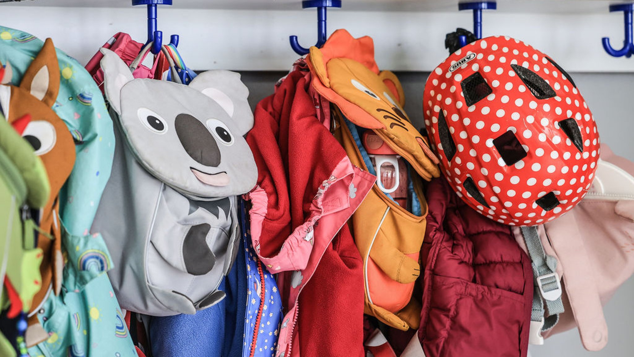 ARCHIV - 03.08.2023, Nordrhein-Westfalen, Düsseldorf: Garderobe und Taschen von Kindern hängen im Flur einer Kindertagesstätte. Das Land will das erfolgreiche Kita-Helfer-Programm bis 2026 verlängern, wird aber die Fördersummen verändern. Manche Einrichtung wird dadurch weniger Geld bekommen. (Zu dpa: «Kita-Helfer-Programm wird bis 2026 verlängert - Kritik wegen Geld») Foto: Oliver Berg/dpa +++ dpa-Bildfunk +++