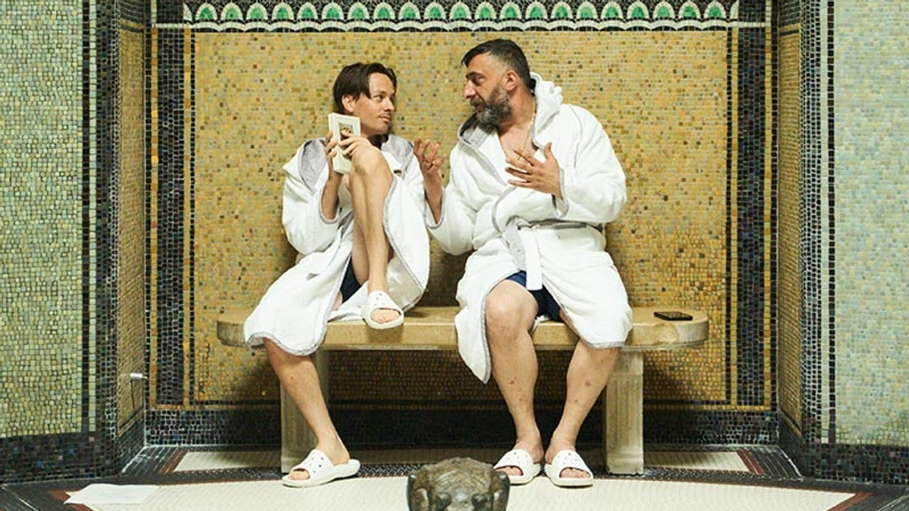 Spielen sich selbst: Tom Schilling als Tom Schilling und Kida Khodr Ramadan als Kida Khodr Ramadan in weißen Bademänteln auf einer Bank in einem Hallenbad in "German Genius"