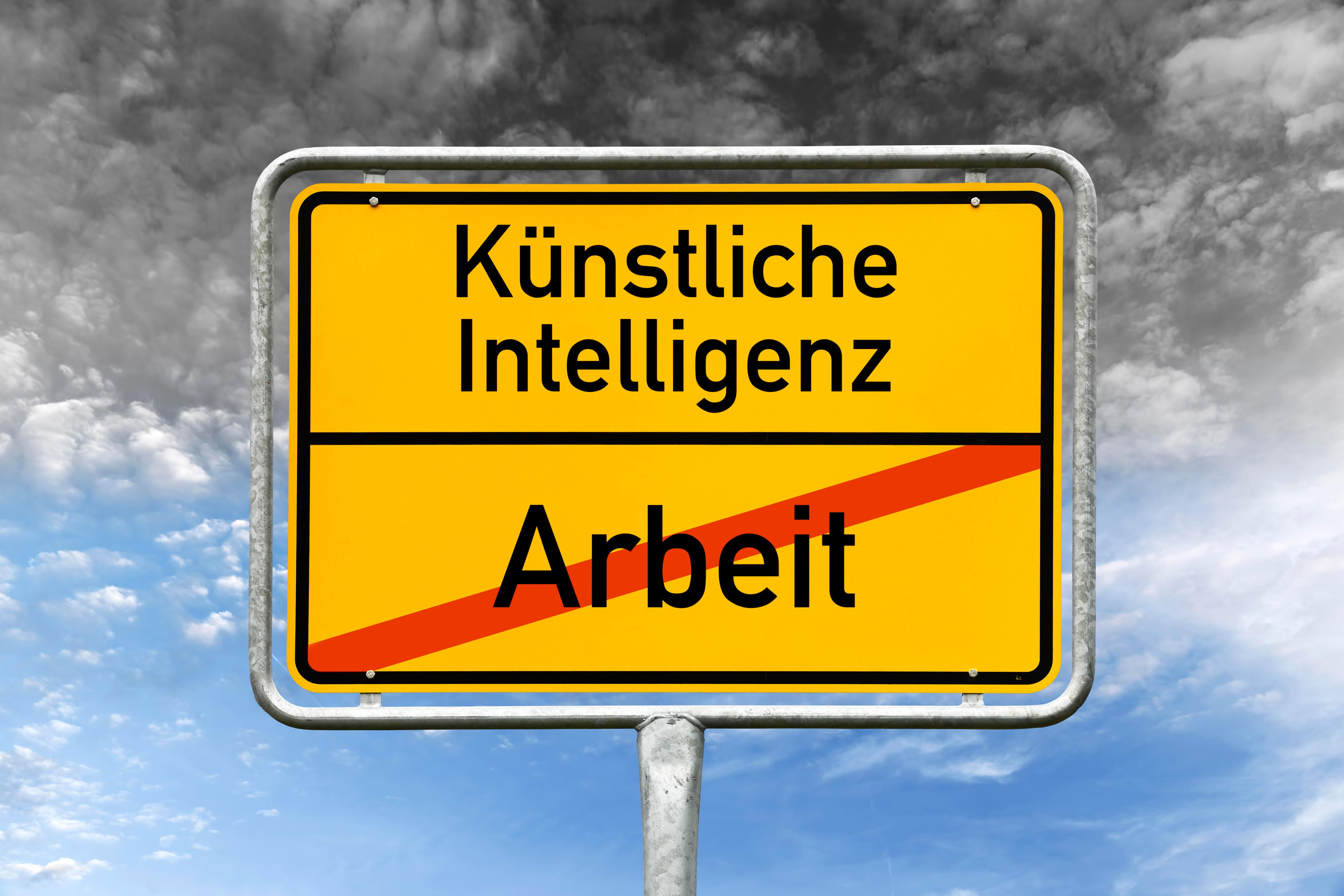 (Symbolbild) Ein Ortsschild, auf dem das Wort "Arbeit" durchgestrichen ist. Darüber steht "Künstliche Intelligenz".