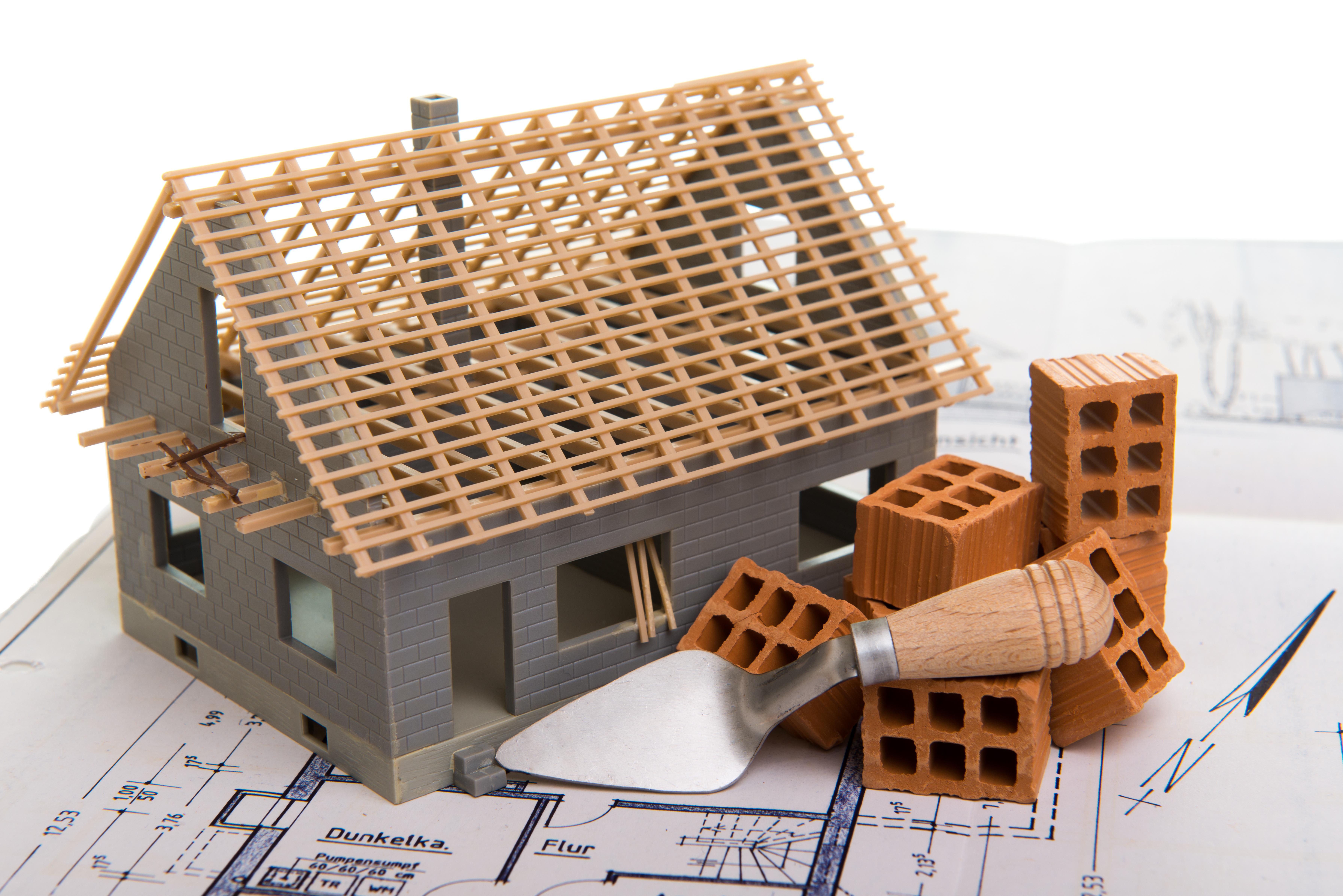 Modell Eines Hausrohbaus mit Ziegeln auf einem Bauplan.