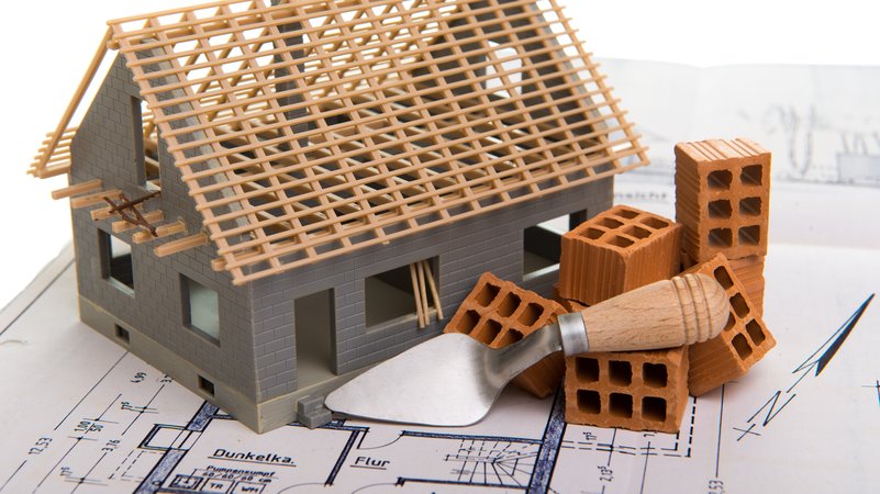 Modell Eines Hausrohbaus mit Ziegeln auf einem Bauplan. | Bild: stock.adobe.com/Gerhard Seybert Modell Eines Hausrohbaus mit Ziegeln auf einem Bauplan.