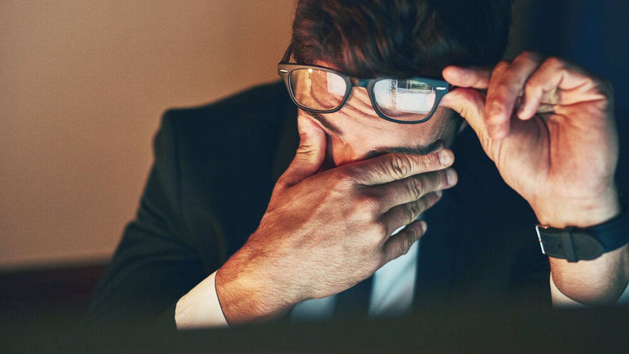 Symbolbild: Ein Mann im Anzug sitzt gestresst vor dem Computer und reibt sich die Augen.