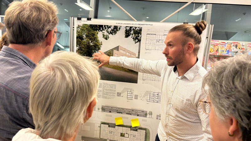 Bürgerinnen und Bürger schauen sich die Pläne zum Neubau des Landsberger Klinikums auf einer Tafel an | Bild: BR / Robert Glawatz Bürgerinnen und Bürger schauen sich die Pläne zum Neubau des Landsberger Klinikums auf einer Tafel an