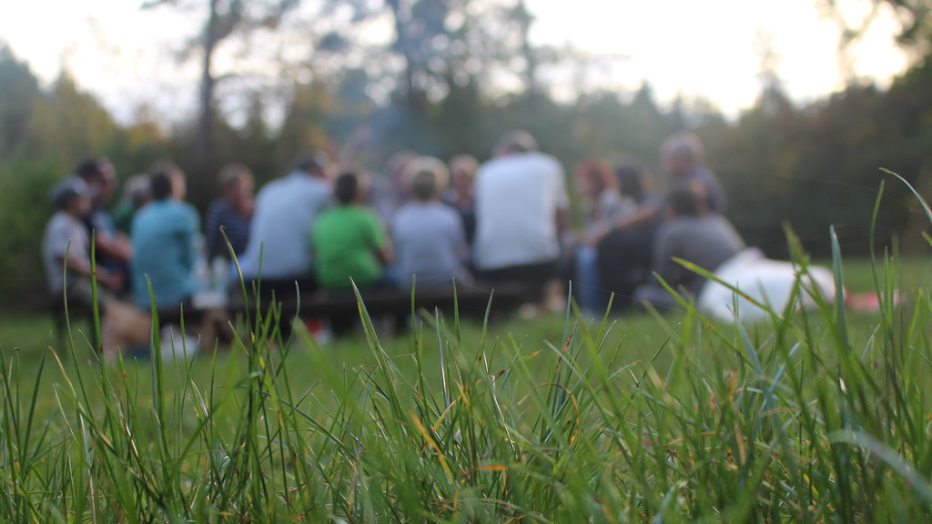 Eine Gruppe Kinder und Erwachsene sitzen im Gras 