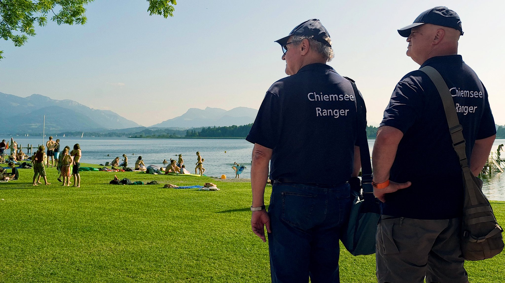 Die Chiemsee-Ranger stehen am Chiemsee und blicken auf die Menschenmenge am Ufer.