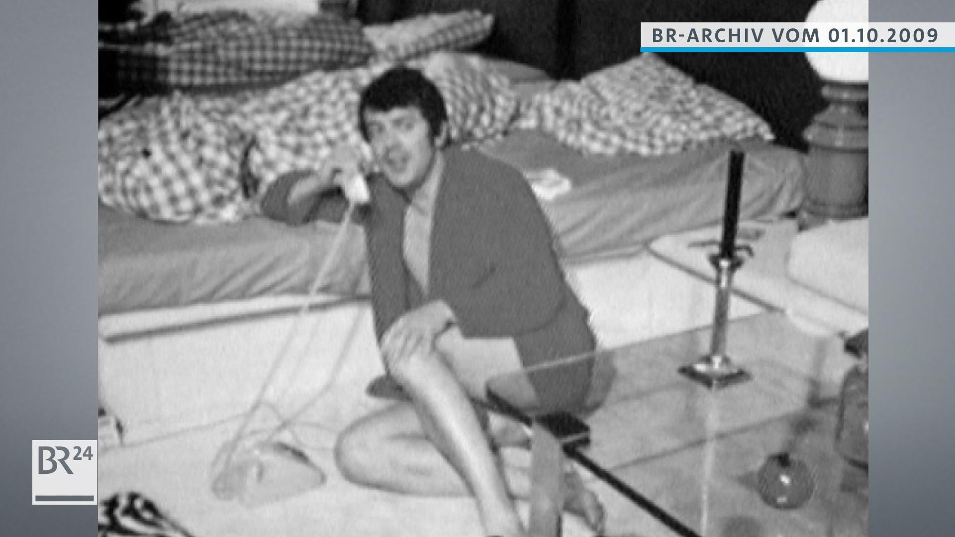 Michael Graeter, mit Bademantel auf dem Boden sitzend, telefoniert mit Festnetz-Wählscheibentelefon