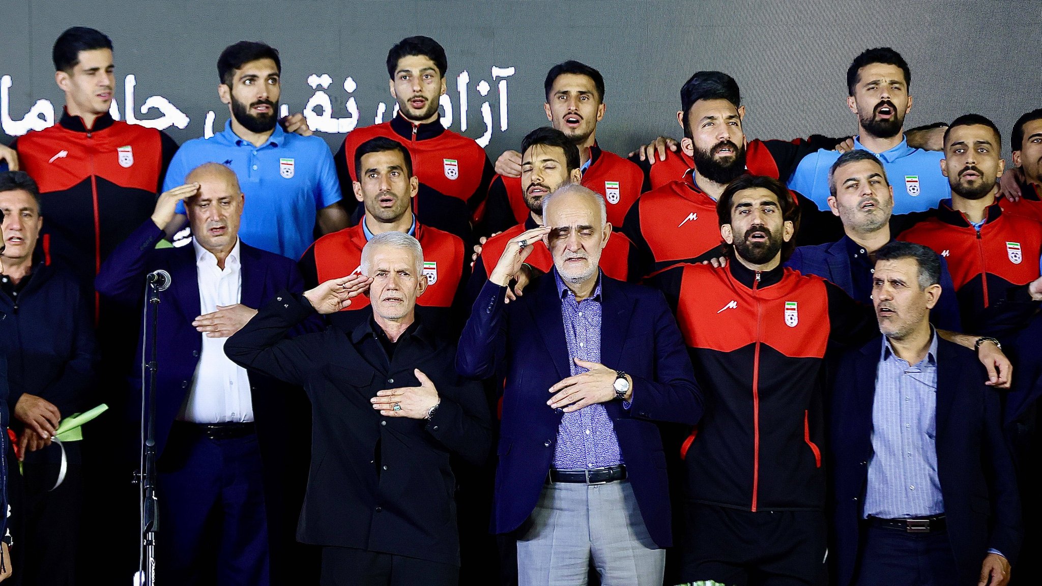 (Symbolbild) Spieler und Vertreter der iranischen Fußballnationalmannschaft stehen auf der Bühne, während sie den militärischen Gruß ausführen. | Bild: picture alliance / SIPA | Hossein/MEI (Symbolbild) Spieler und Vertreter der iranischen Fußballnationalmannschaft stehen auf der Bühne, während sie den militärischen Gruß ausführen.