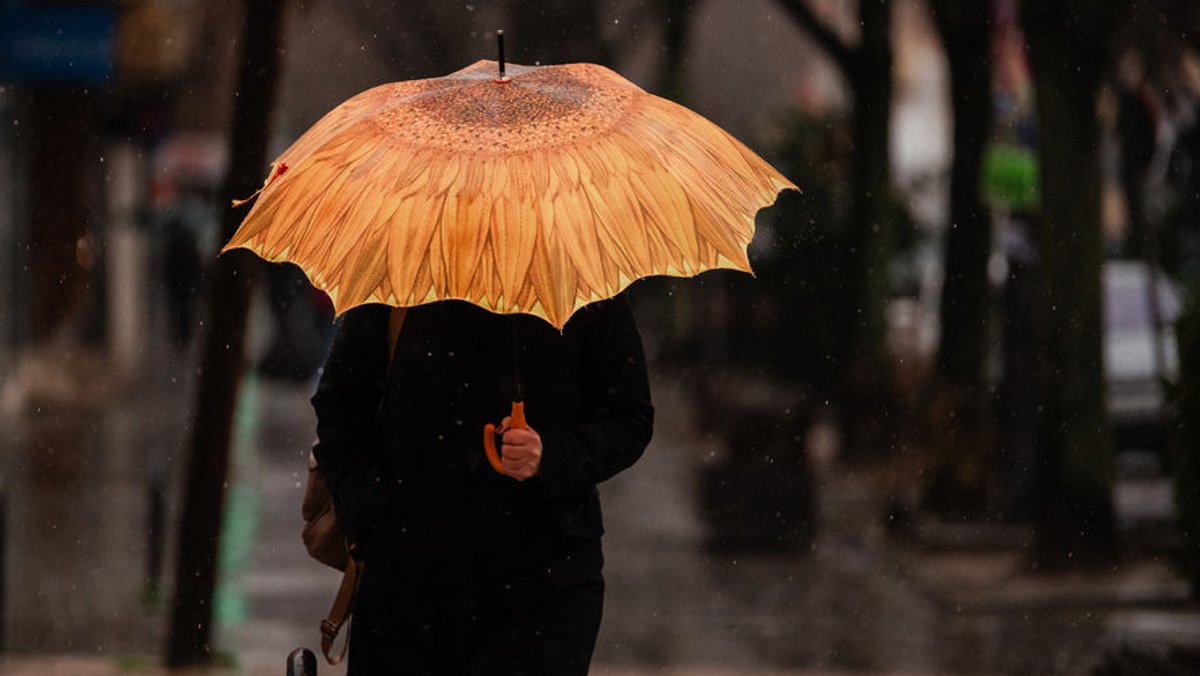 Eine Person trägt einen gelben Regenschirm (Symbolbild).