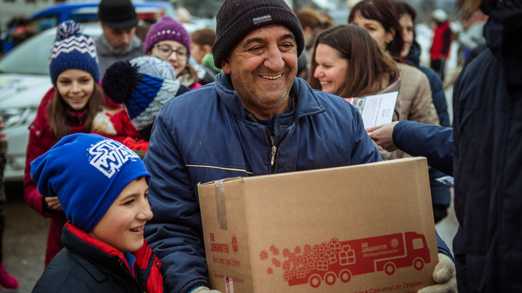 Ein Mann und ein Kind freuen sich über ein Paket der Johanniter "Weihnachtstrucker"