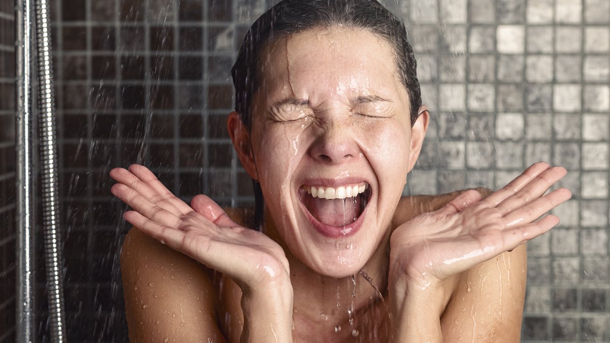 Frau steht mit Grimasse unter einer Dusche | Bild: picture alliance / Zoonar | Lars Zahner Frau steht mit Grimasse unter einer Dusche
