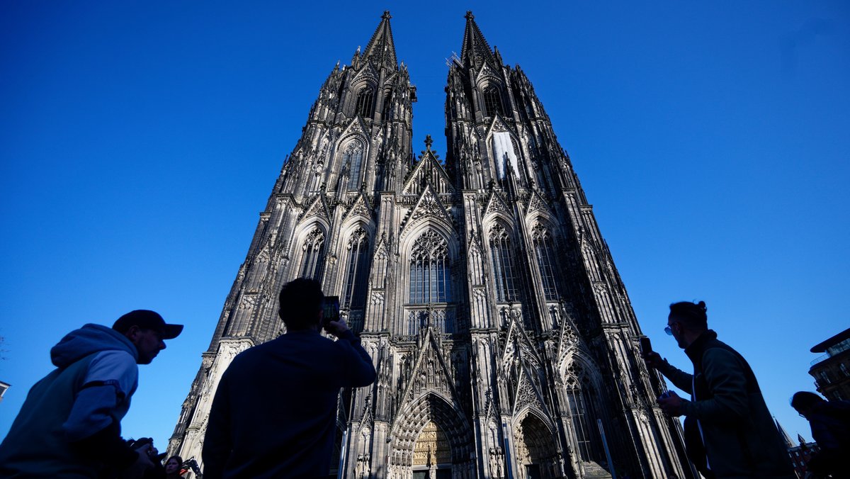 ARCHIV - 05.03.2026, Nordrhein-Westfalen, Köln: Touristen fotografieren den Kölner Dom. Der Kölner Dom wird Touristen in Zukunft Eintritt kosten. Damit sollen die gestiegenen Kosten für Pflege, Schutz und den laufenden Betrieb des Doms gedeckt werden, wie das Domkapitel mitteilte. (zu dpa: «Von Ablehnung bis Verständnis - Promis zum Dom-Eintritt») Foto: Henning Kaiser/dpa +++ dpa-Bildfunk +++ | Bild: dpa-Bildfunk/Henning Kaiser ARCHIV - 05.03.2026, Nordrhein-Westfalen, Köln: Touristen fotografieren den Kölner Dom. Der Kölner Dom wird Touristen in Zukunft Eintritt kosten. Damit sollen die gestiegenen Kosten für Pflege, Schutz und den laufenden Betrieb des Doms gedeckt werden, wie das Domkapitel mitteilte. (zu dpa: «Von Ablehnung bis Verständnis - Promis zum Dom-Eintritt») Foto: Henning Kaiser/dpa +++ dpa-Bildfunk +++