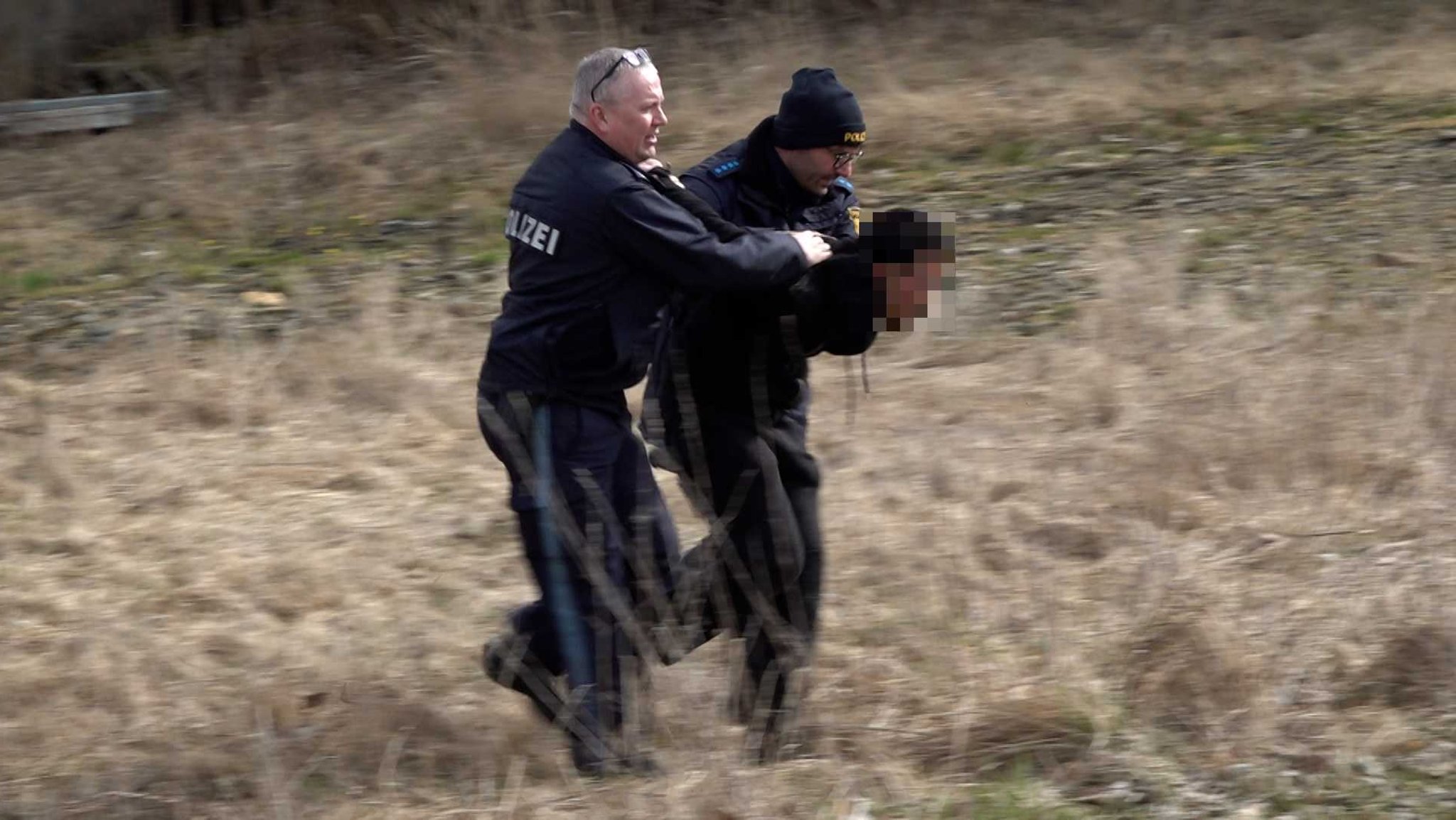 Zwei Polizisten führen eine festgenommene Person ab.