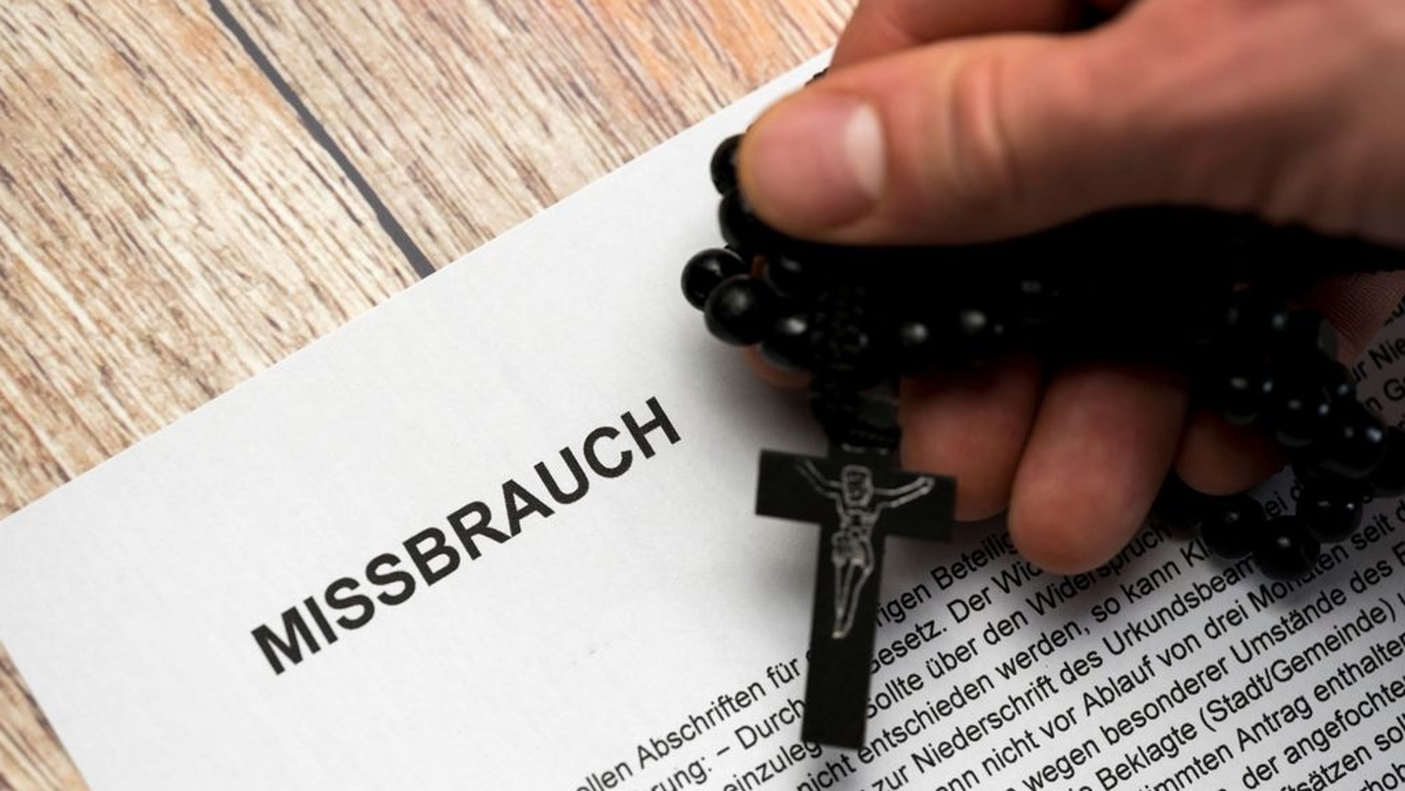 Schriftstück mit Text über Missbrauchsfall und eine Hand mit Rosenkranz