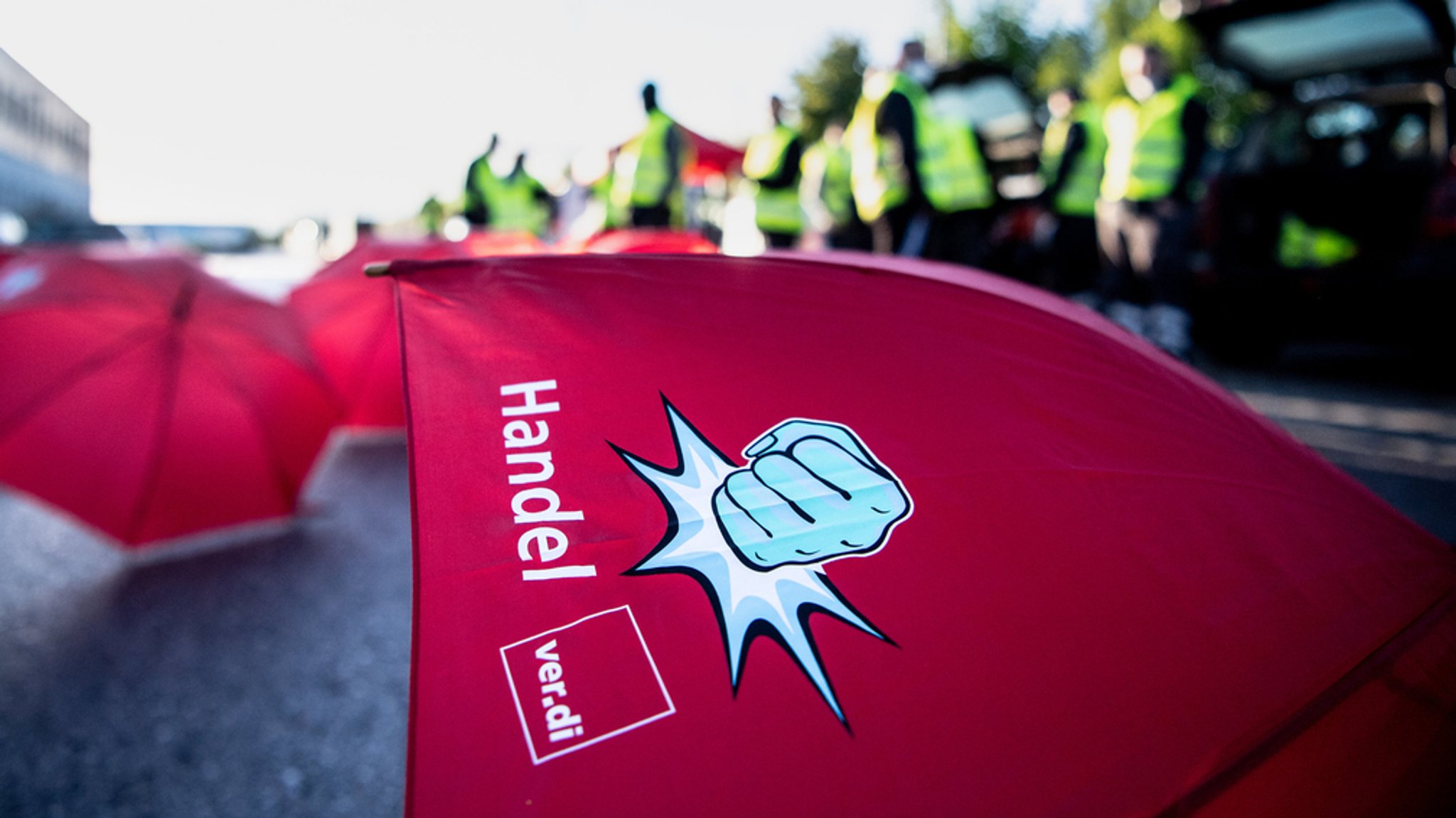 Ein roter Regenschirm liegt auf dem Asphalt. Im Hintergrund Menschen mit Warnwesten.