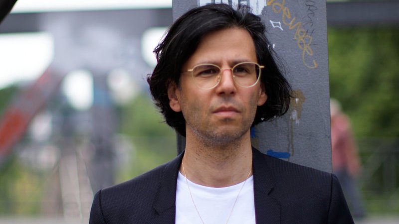 Der Autor Deniz Utlu (schwarze Haare, schlichte Brille) auf der Straße.