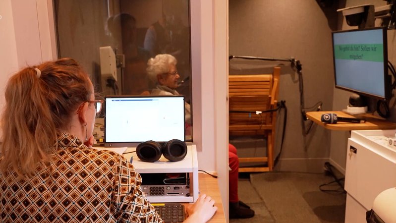 Eine Seniorin spricht gerade in einem Forschungsmobil in ein Mikrophon. 