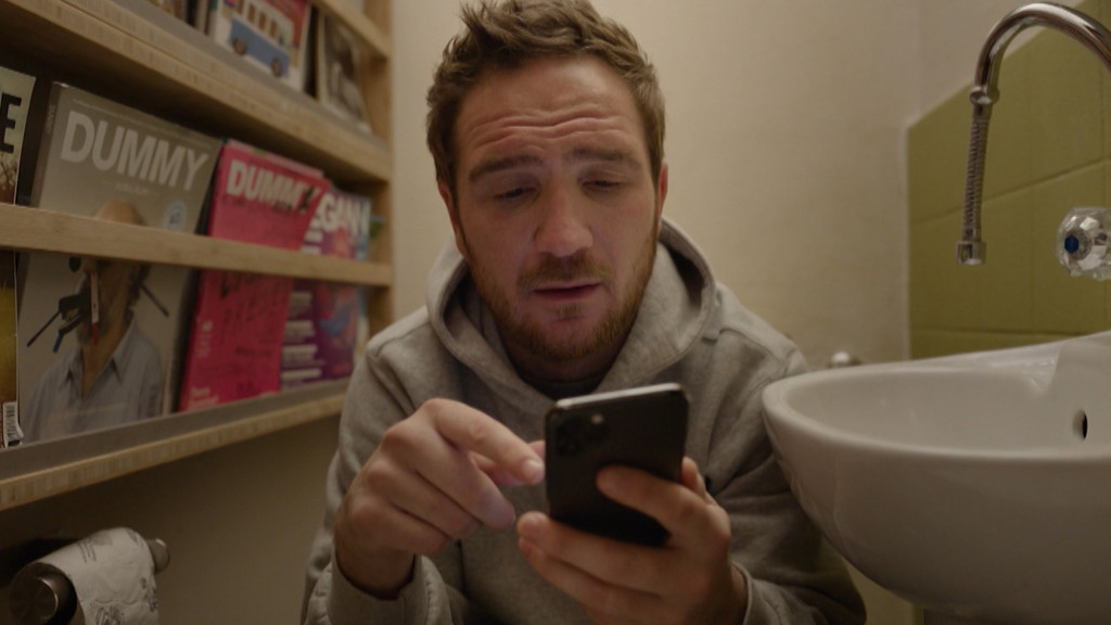 Frederick Lau sitzt offenbar auf einer Toilette und schaut dabei auf sein Handy | Bild: Bayerischer Rundfunk 2021 Frederick Lau sitzt offenbar auf einer Toilette und schaut dabei auf sein Handy