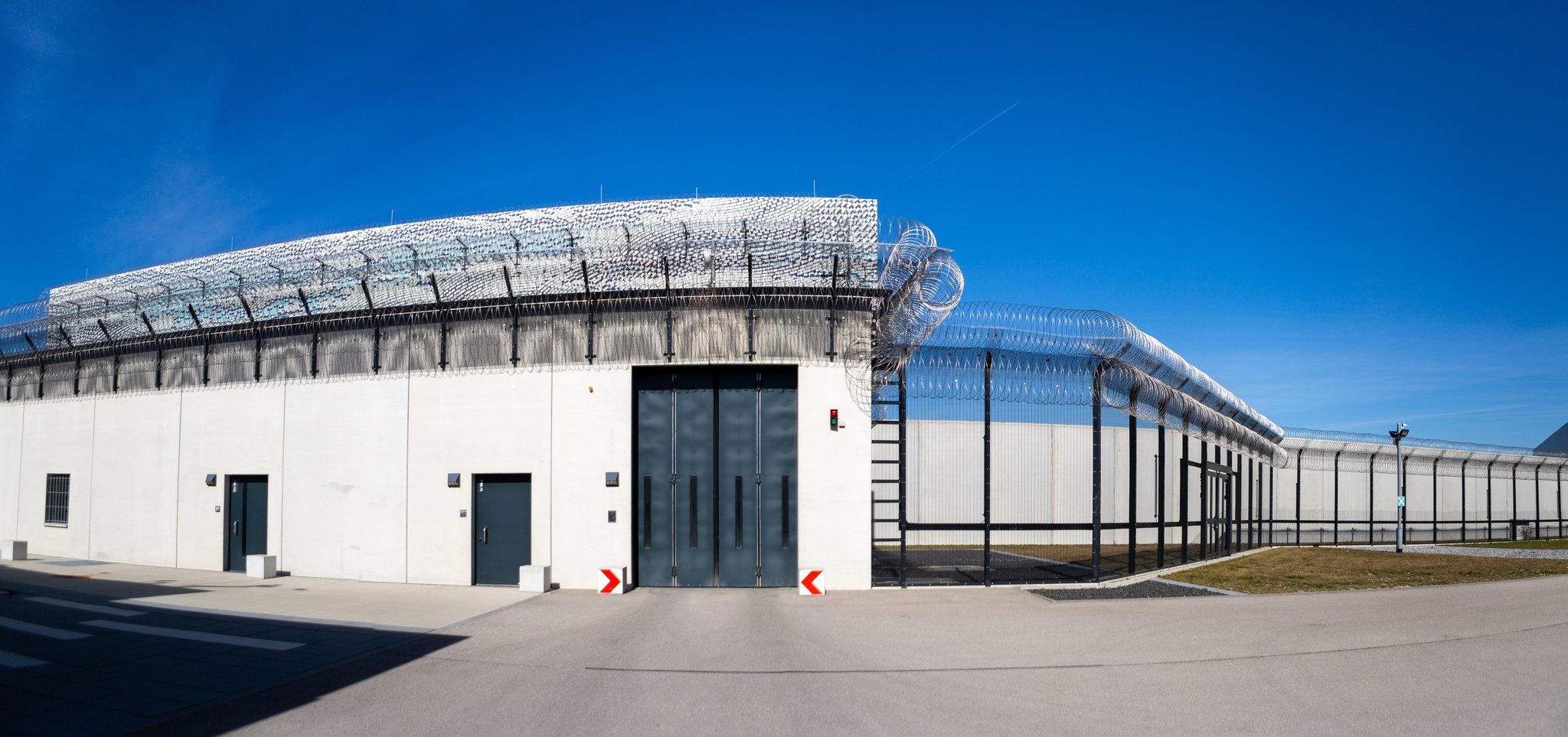 Blick vom Hof eines Gefängnisses auf die Gefängnismauern mit Stacheldraht.