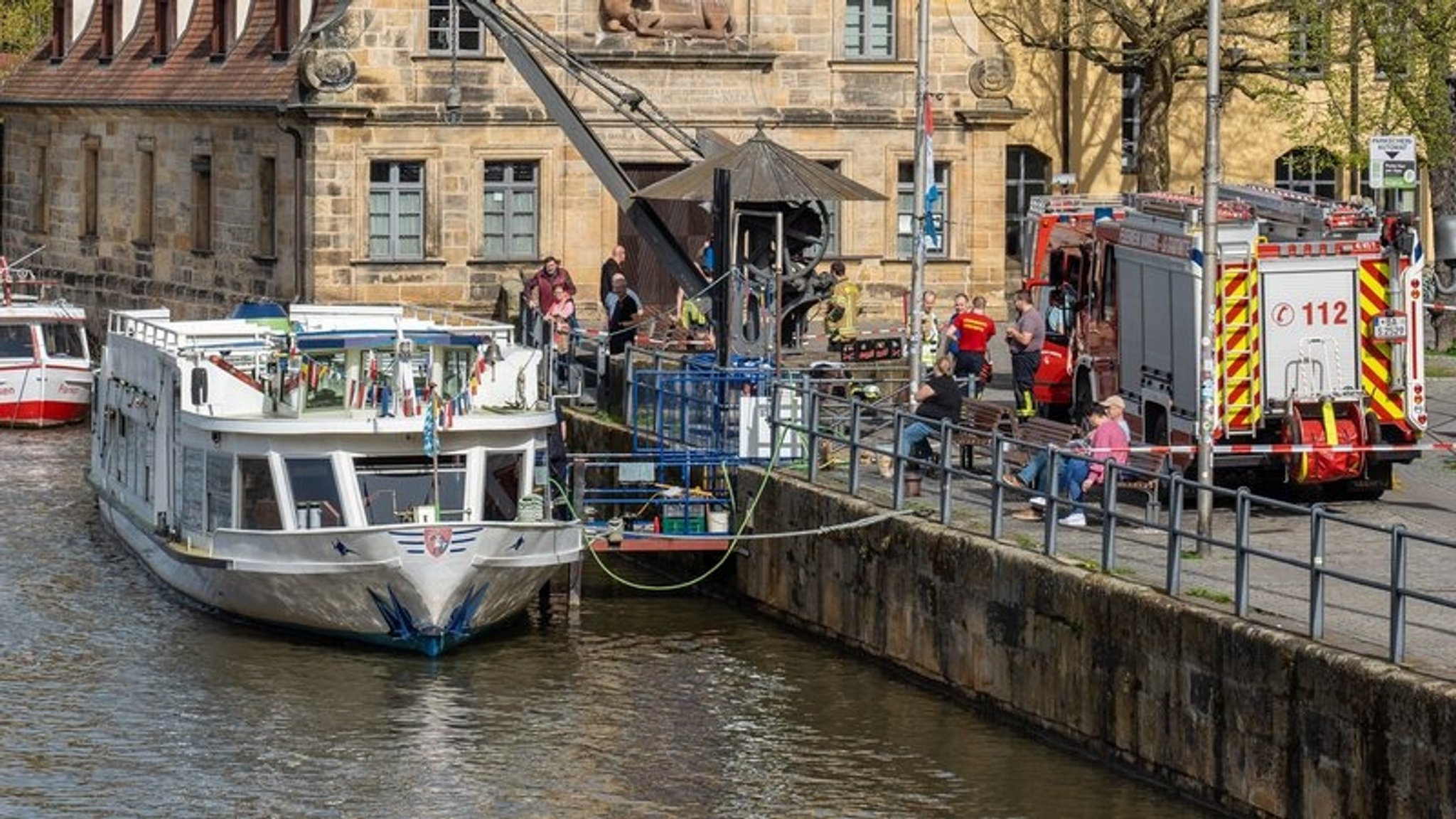 Ein Personenschiff liegt im Wasser. An Land steht ein Feuerwehrfahrzeug. 