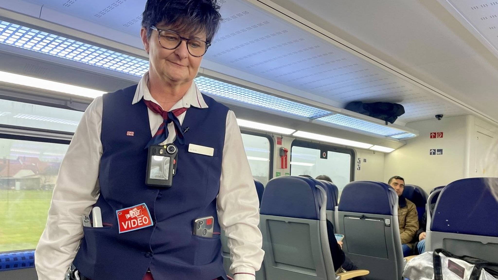 Eine Zugbegleiterin der Bahn in blauer Uniform trägt eine Bodycam am Oberkörper.