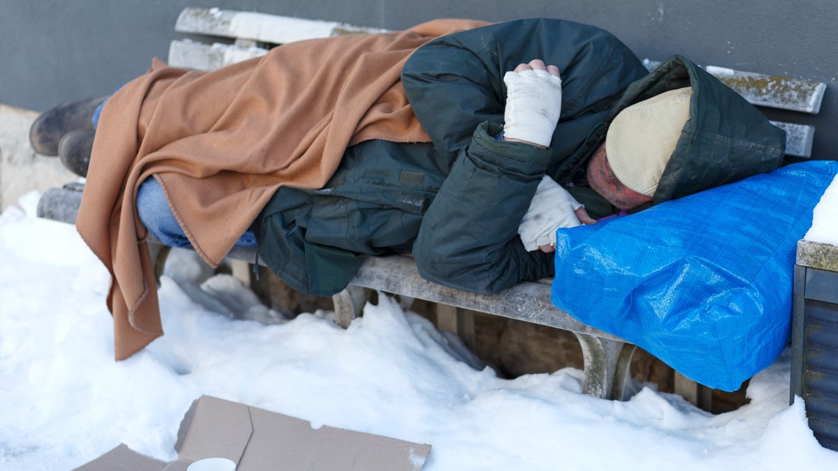 Obdachloser Mann schläft im Winter auf einer Parkbank